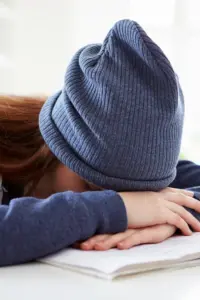 Woman Wearing Blue Hat With Hands On Forehead On Desk